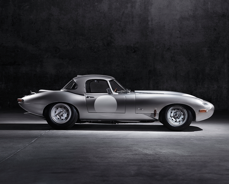 Blue Jaguar E-Type convertible in a dimly lit setting.