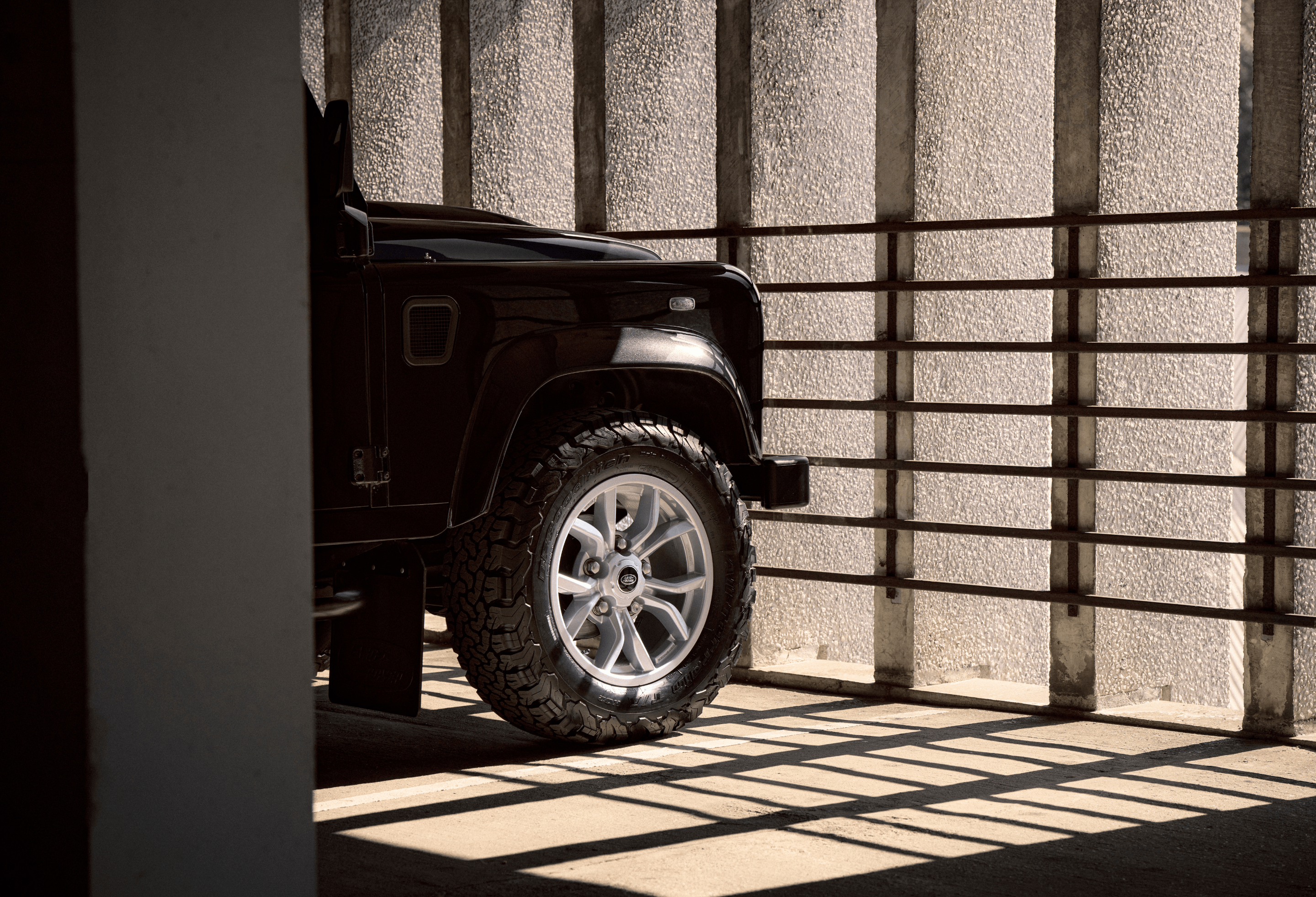Front right tire of a black Defender in a shadowed concrete setting.